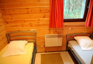Værelse i chalet De Boshut i Belgien med to enkeltsenge, trævægge og vindue med udsigt til skov.