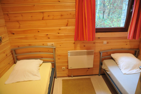 Chambre au chalet De Boshut en Belgique avec deux lits simples, murs en bois et vue sur la forêt.