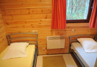 Chambre au chalet De Boshut en Belgique avec deux lits simples, murs en bois et vue sur la forêt.