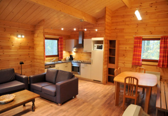 Interior of a cozy wooden chalet named 'De Boshut' in Belgium featuring a kitchen, dining, and lounge area.