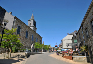 Gadebillede i Belgien set fra De Boshut-chalet med stenhuse, en kirke og et udendørs caféområde.