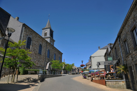 Vue de rue en Belgique depuis le chalet De Boshut montrant des maisons en pierre, une église et un café extérieur.