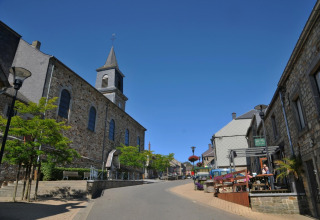 Vue de rue en Belgique depuis le chalet De Boshut montrant des maisons en pierre, une église et un café extérieur.
