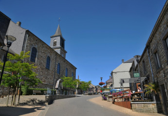 Street view in Belgium from De Boshut chalet, showing stone buildings, a church, and an outdoor café.
