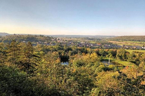 Udsigt over frodigt landskab og lille sø fra glamping-ophold med by i baggrunden under klar himmel.