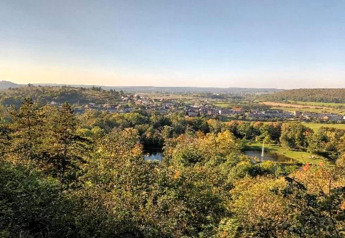 Blick auf eine grüne Landschaft mit Teich und Dorf im Hintergrund, gesehen von einer Glamping-Unterkunft.