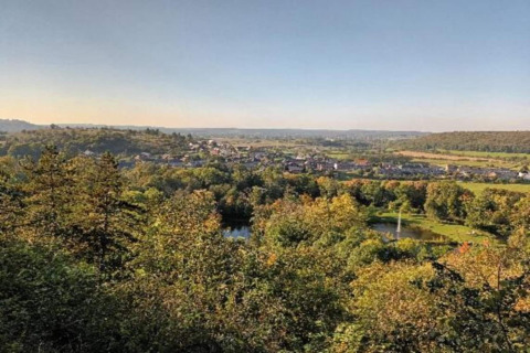 Scenic view from a glamping site showing lush green trees, a small pond, and a village in the distance.