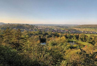 Vue depuis un hébergement glamping sur un paysage verdoyant avec un étang et un village en arrière-plan.