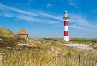 Een rood-wit gestreepte vuurtoren en een huisje in de duinen bij Nieuwpoort, België, onder een blauwe lucht.