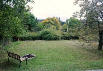 Blick auf einen grünen Garten mit Feuerstelle und Bank bei einer Glamping-Unterkunft im Grünen.