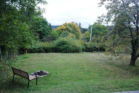 Vue d’un hébergement glamping sur une pelouse avec un banc près d’un foyer et des arbres verdoyants.