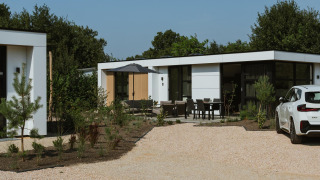 Moderne lodge Villa Bloomingdale Wellness met buitenterras, tuinmeubilair en een witte auto op de oprit.