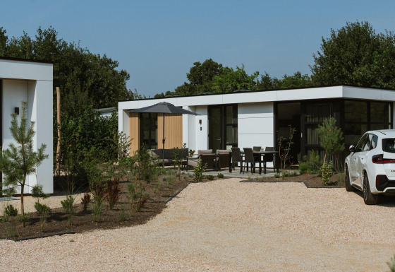 Moderne lodge Villa Bloomingdale Wellness met buitenterras, tuinmeubilair en een witte auto op de oprit.