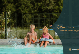 Twee kinderen spetteren bij het buitenzwembad van een glamping accommodatie op een zonnige dag.