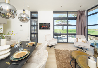 Salón moderno de lodge con mesa de comedor, Netflix en la TV, sillones cómodos y vista a campos verdes.