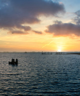 Sunset view over the sea at a holiday park with glamping, lighthouse to the right, dramatic sky above.