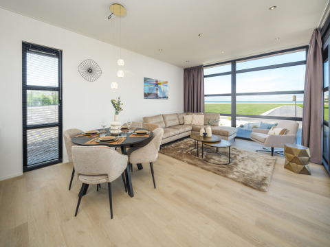 Modernes Wohnzimmer einer Lodge mit großen Fenstern, Essbereich, Sofa und Ausblick aufs Grün.