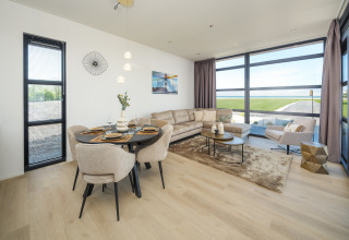 Modernes Wohnzimmer einer Lodge mit großen Fenstern, Essbereich, Sofa und Ausblick aufs Grün.