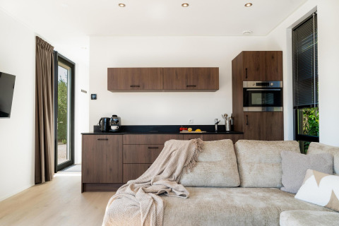 Moderne lodge met gezellige beige bank, compacte keuken in hout, grote ramen en veel daglicht.