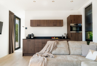 Moderne lodge met gezellige beige bank, compacte keuken in hout, grote ramen en veel daglicht.