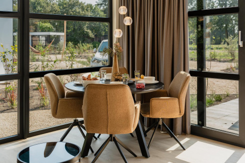 Gezellige eethoek in een lodge met vier stoelen, ronde tafel, grote ramen en uitzicht op de natuur.