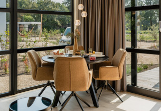 Gezellige eethoek in een lodge met vier stoelen, ronde tafel, grote ramen en uitzicht op de natuur.