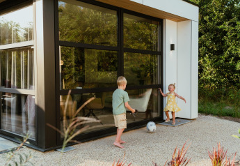 Zwei Kinder spielen mit einem Fußball vor einer modernen Lodge mit großen Fenstern und viel Grün.
