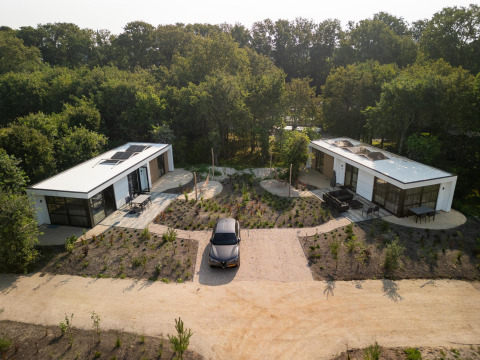 Luchtfoto van een lodge met twee moderne huisjes, auto ertussen, omringd door bomen en natuur.