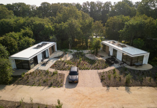 Luchtfoto van een lodge met twee moderne huisjes, auto ertussen, omringd door bomen en natuur.