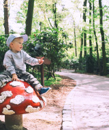 Petit garçon assis sur un grand champignon décoratif près d’un sentier forestier dans un parc de glamping.