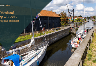 Voiliers naviguant sur un canal près de bâtiments historiques et d'un glamping à Friesland, Pays-Bas.