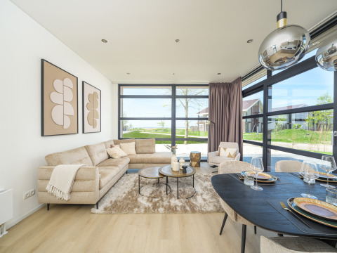 Modern lodge living room with large windows, beige sofa, dining table and a view of the garden.