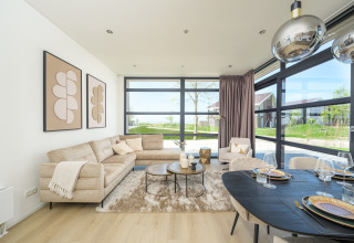 Modern lodge living room with large windows, beige sofa, dining table and a view of the garden.