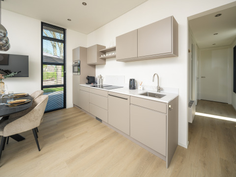 Modern lodge kitchen with beige cabinets, wood flooring, dining area, and large window with garden view.