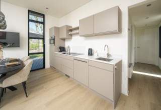 Modern lodge kitchen with beige cabinets, wood flooring, dining area, and large window with garden view.