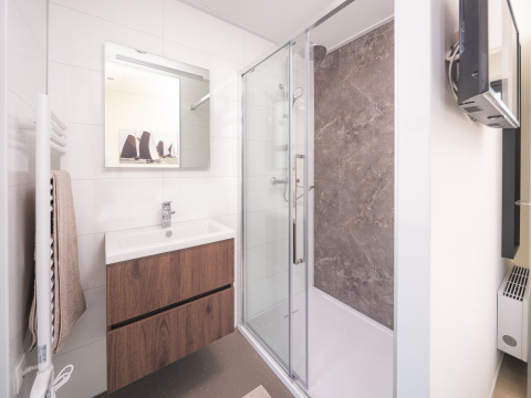 Modern lodge bathroom with glass shower, wooden vanity, wall mirror, and towel rack on white tiles.