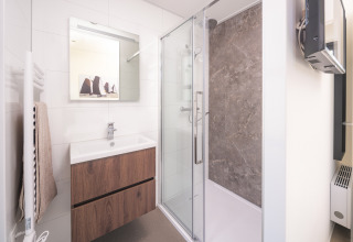 Modern lodge bathroom with glass shower, wooden vanity, wall mirror, and towel rack on white tiles.