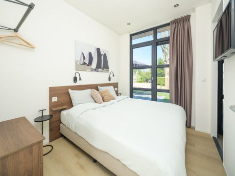 Modern lodge bedroom with double bed, large windows, light wood flooring, and minimalist decor.