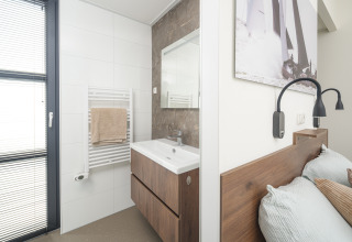Modern lodge interior showing a bathroom with sink and bedroom area, separated by a partial wall.