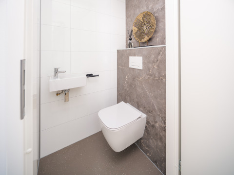 Modern lodge bathroom with wall-hung toilet, compact sink, decorative art piece, and marble accent wall.