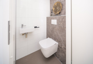 Modern lodge bathroom with wall-hung toilet, compact sink, decorative art piece, and marble accent wall.