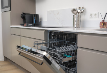 Cocina moderna en una cabaña con lavavajillas abierto, electrodomésticos y utensilios en la encimera.