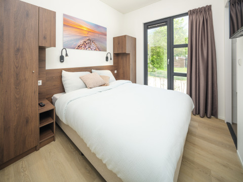 Modernes Schlafzimmer in einer Lodge mit großem Bett, Holzmöbeln und Fenster mit Gartenblick.