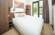 Chambre moderne d’un lodge avec grand lit, meubles en bois et porte-fenêtre donnant sur le jardin.