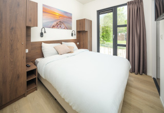 Camera moderna in un lodge con letto grande, mobili in legno e vista sul giardino verde dal balcone.