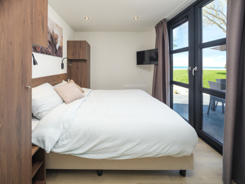 Modernes Lodge-Schlafzimmer mit großem Fenster, Doppelbett, Wandkunst und Blick ins Grüne.