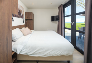 Modernes Lodge-Schlafzimmer mit großem Fenster, Doppelbett, Wandkunst und Blick ins Grüne.