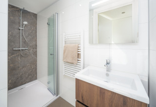 Salle de bain moderne de lodge avec douche vitrée, meuble en bois, miroir éclairé et serviette suspendue.