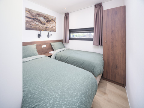Modernes Lodge-Zimmer mit zwei Einzelbetten, grüner Bettwäsche, Wandkunst und Gardinen am Fenster.