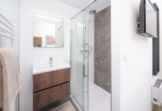 Salle de bain moderne en lodge avec douche en verre, meuble en bois, miroir et télévision murale.